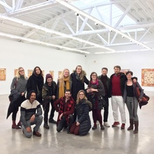 12 people gather in a white room with artwork on the walls