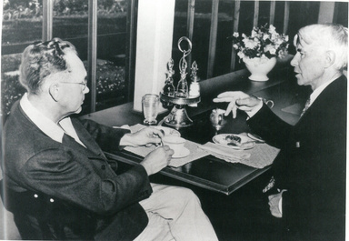 Grant Wood sitting across the table from author Carol Sandburg over tea.