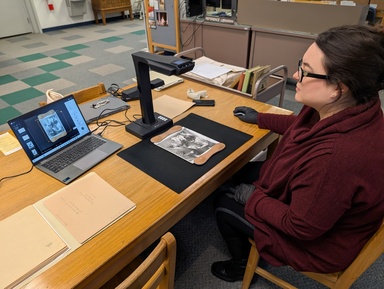 woman sits at a desk with a laptop and scanner