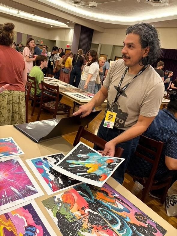 man showing prints of his artwork at a table during a well-attended event