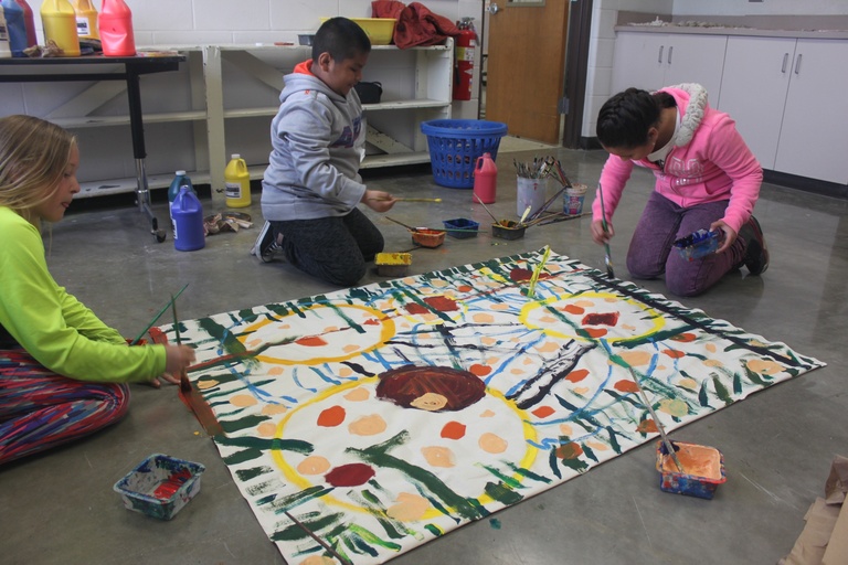 children paint bright abstract marks on a canvas laid on the ground