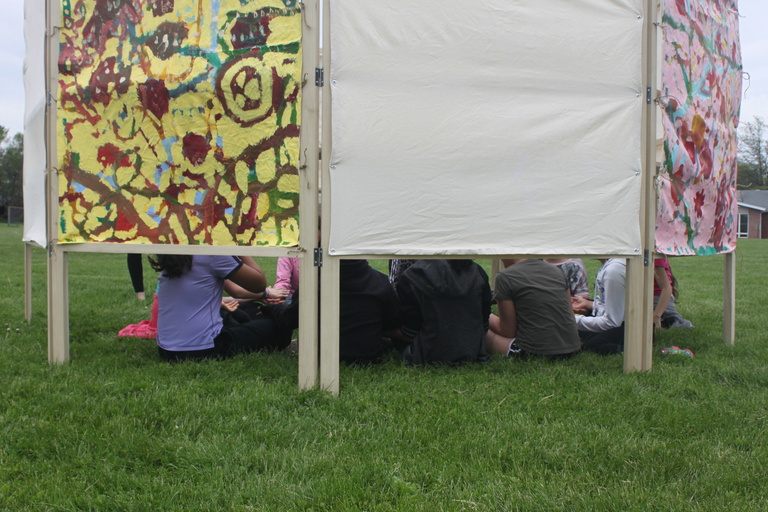 children sit behind a canvas screen outside
