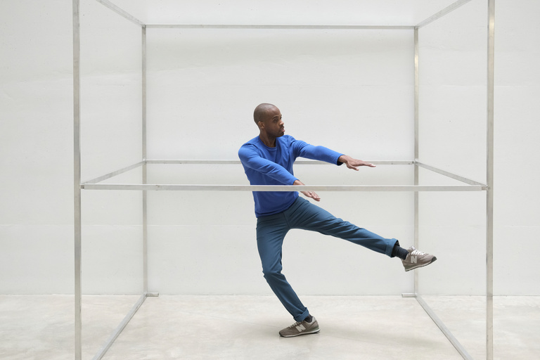 a man in blue shirt and pants stands in a metal open cube