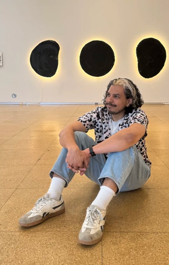 white man sits on the floor in front of three black blobs