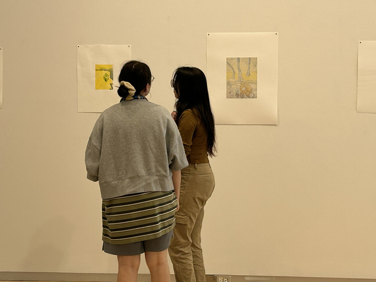 two women look at colorful prints on the white wall