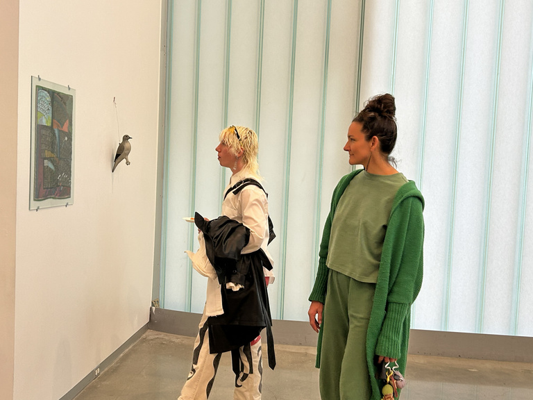 two people look at artwork displayed on a white wall