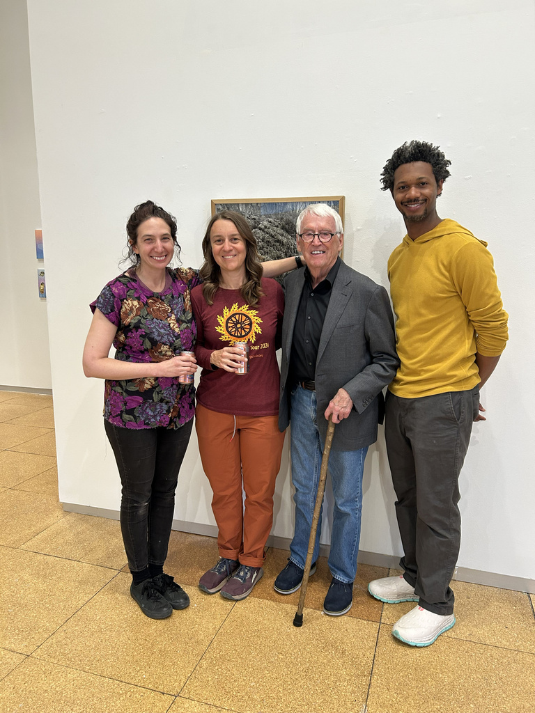 four people stand smiling in front of a white wall