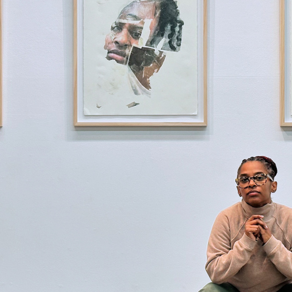 TJ Dedeaux-Norris squatting in front three framed examples of their collage artwork