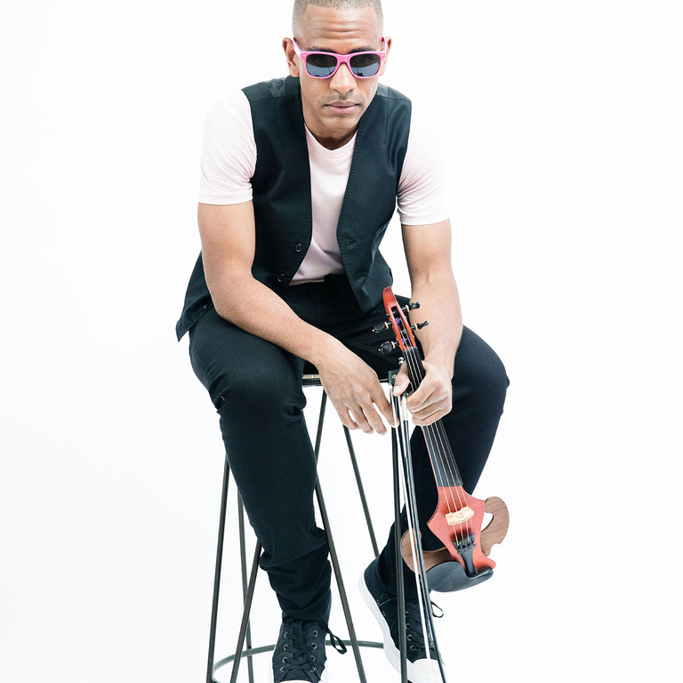 Josh Henderson holding a violin while sitting on a stool