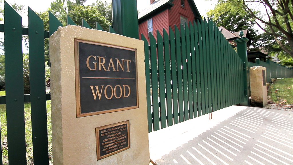 Green fence with metal plaque at the front gate of the Grant Wood Art Colony property mentioning the donors.