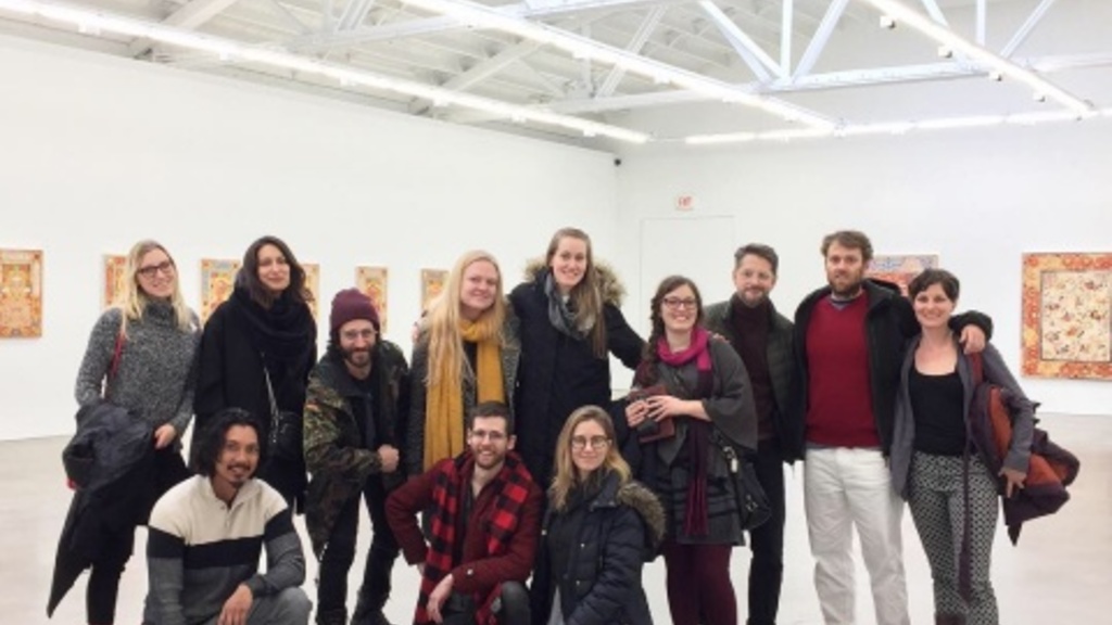 12 people gather in a white room with artwork on the walls