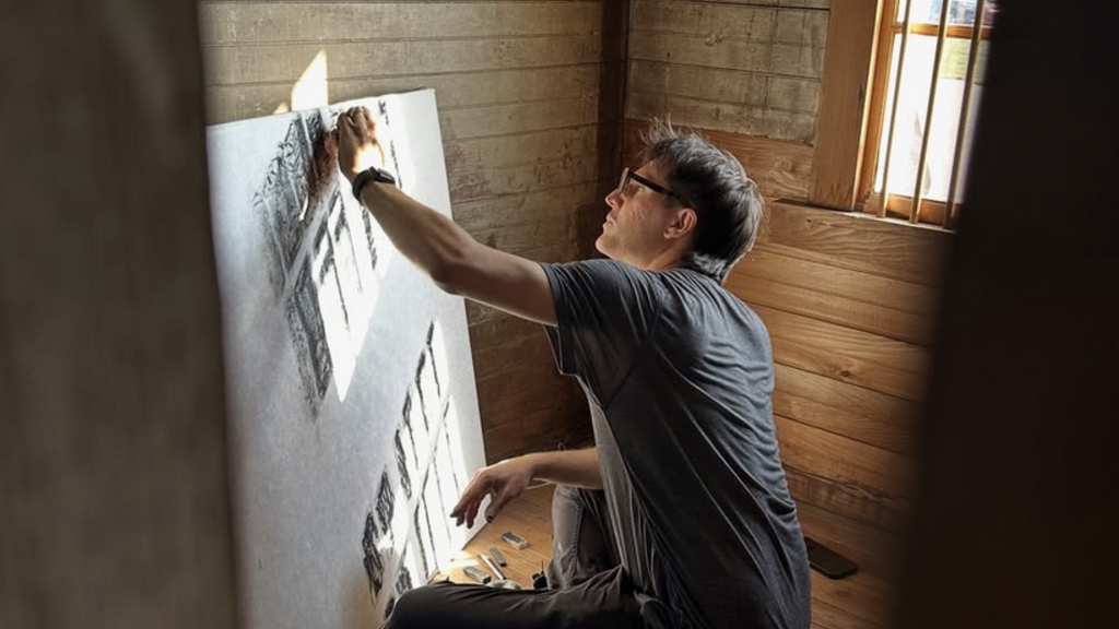 a man sits on the floor drawing on a white board in a wooden room